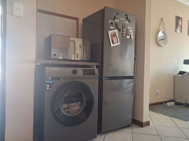 A functional laundry nook featuring a stone countertop, tiled flooring, and dedicated space for a washing machine and refrigerator.