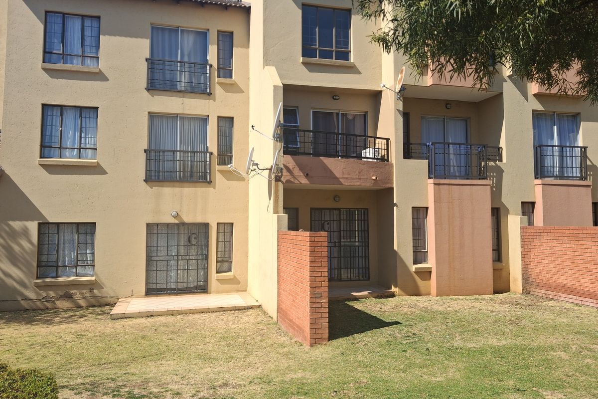 Rear view of a multi-story townhouse complex featuring private balconies, ground floor patios, security gates, and shared garden space.