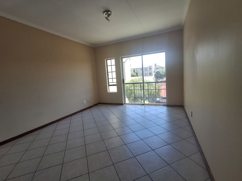 An empty living room featuring tiled flooring, a sliding glass door with security gate, and natural light, ready for personalization.