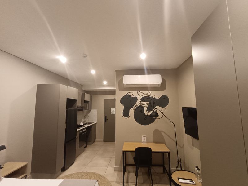 Modern open-plan apartment living area featuring a compact kitchen with built-in cabinetry, integrated appliances, and a split-system air conditioner.