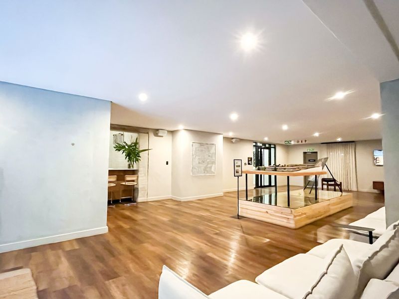 A spacious, well-lit clubhouse area featuring modern laminate flooring, recessed ceiling lighting, and a built-in bar counter, suitable for communal gatherings.