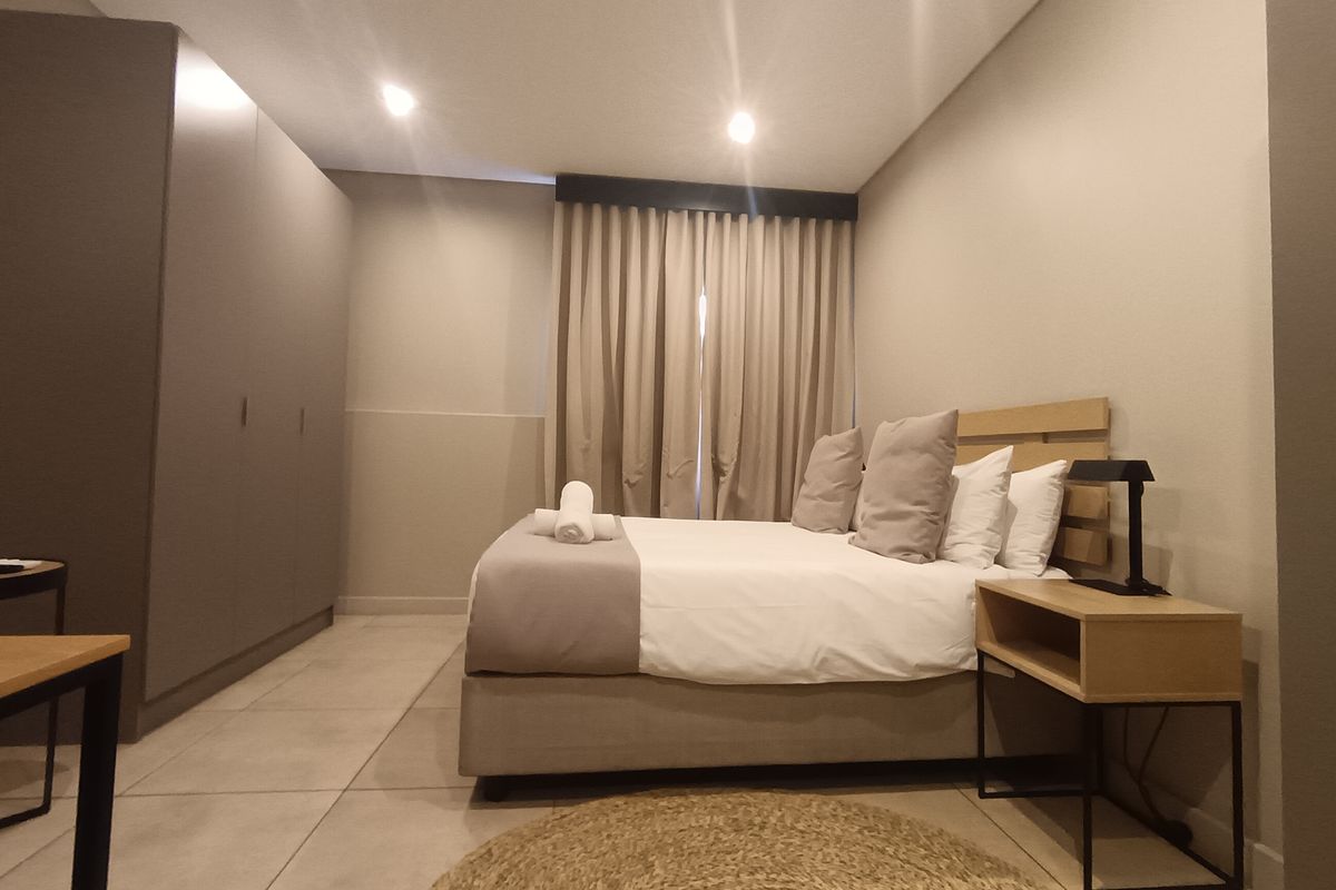 A modern, well-maintained bedroom featuring neutral tones, tiled flooring, recessed ceiling lighting, and a large built-in wardrobe.