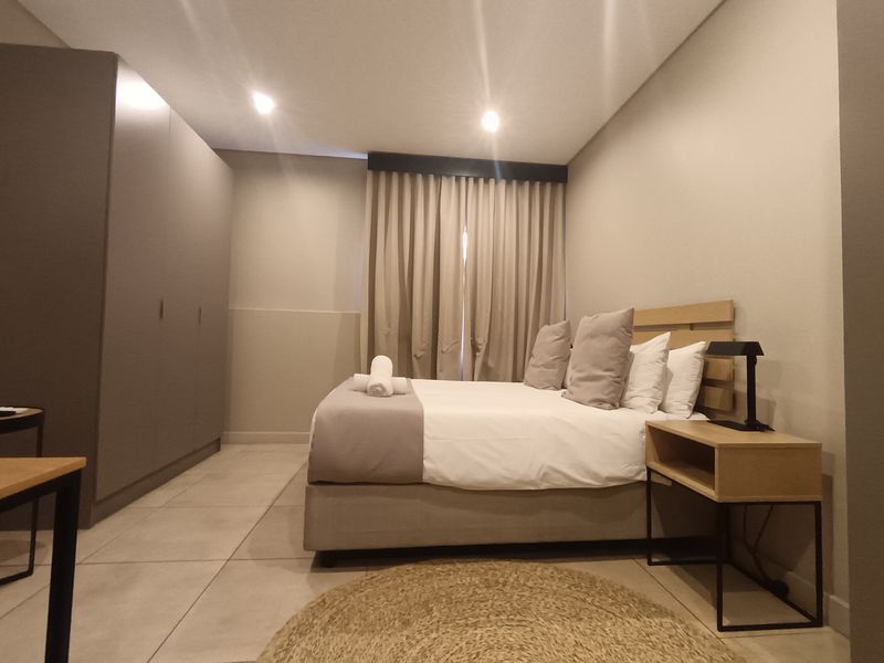 A modern, well-maintained bedroom featuring neutral tones, tiled flooring, recessed ceiling lighting, and a large built-in wardrobe.