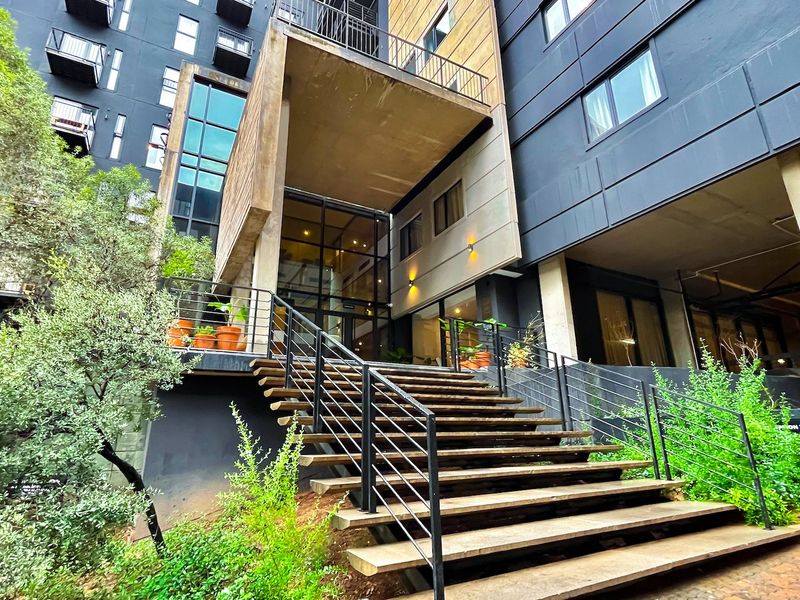 Modern apartment building entrance featuring a prominent concrete staircase, metal railings, and a contemporary glass facade with integrated exterior lighting.