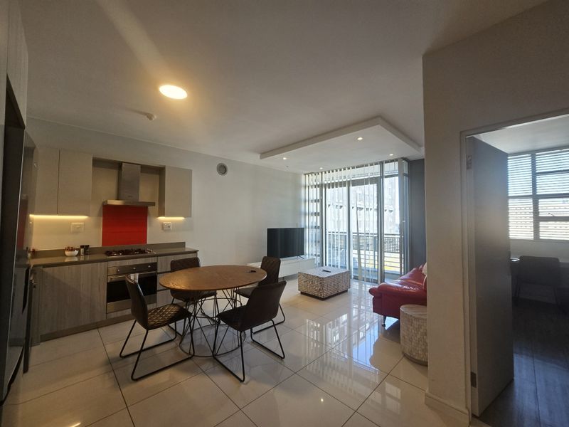Modern open-plan living area featuring a sleek kitchen with built-in appliances, tiled flooring, and large sliding doors leading to a balcony.