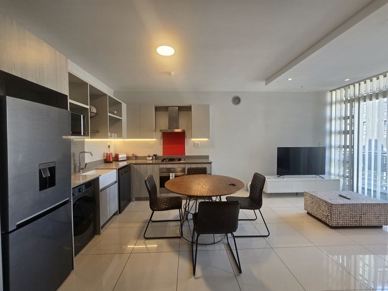 Modern open-plan kitchen and living area featuring sleek cabinetry, integrated appliances, tiled flooring, and large sliding doors leading to a balcony.