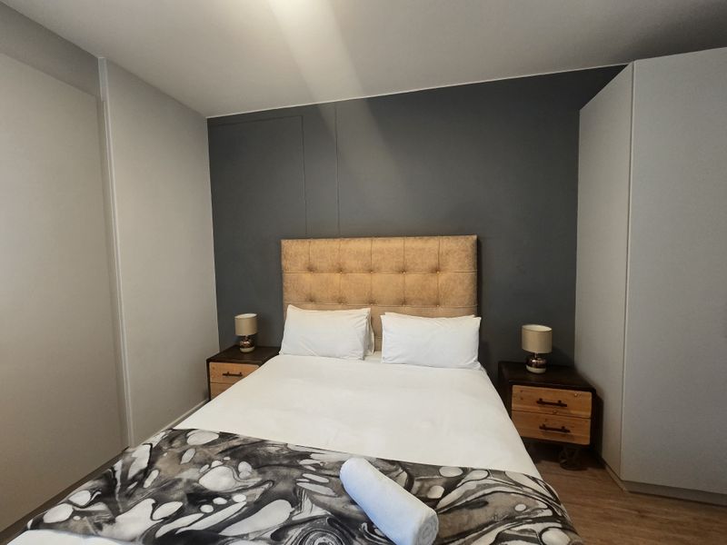 A well-maintained bedroom featuring a dark accent wall, built-in wardrobe storage, and durable laminate flooring.