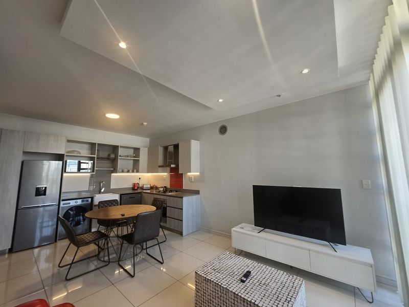 Modern open-plan living area featuring a contemporary kitchen with built-in cabinetry, integrated appliances, and sleek tiled flooring throughout.