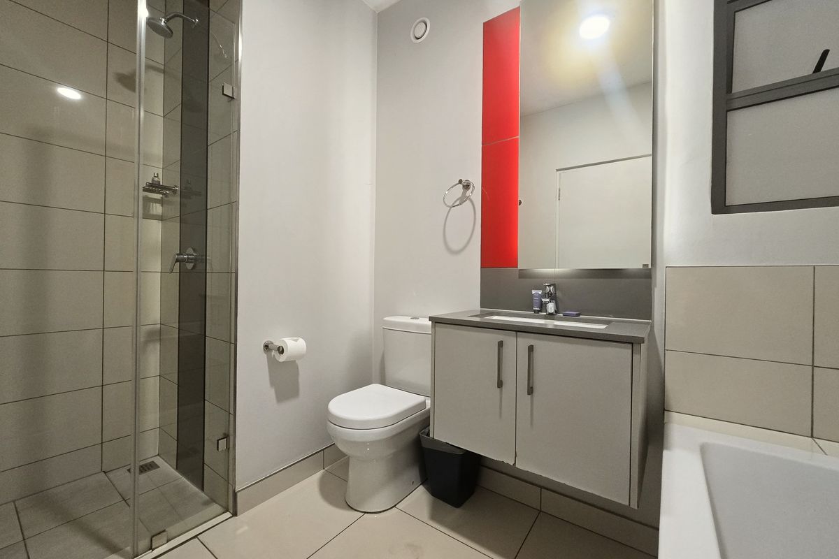 Modern bathroom featuring a glass-enclosed shower, wall-mounted vanity with integrated basin, and neutral floor-to-ceiling tiling with a bold red accent panel.