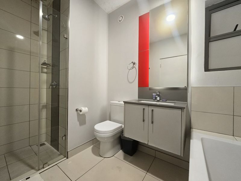 Modern bathroom featuring a glass-enclosed shower, wall-mounted vanity with integrated basin, and neutral floor-to-ceiling tiling with a bold red accent panel.
