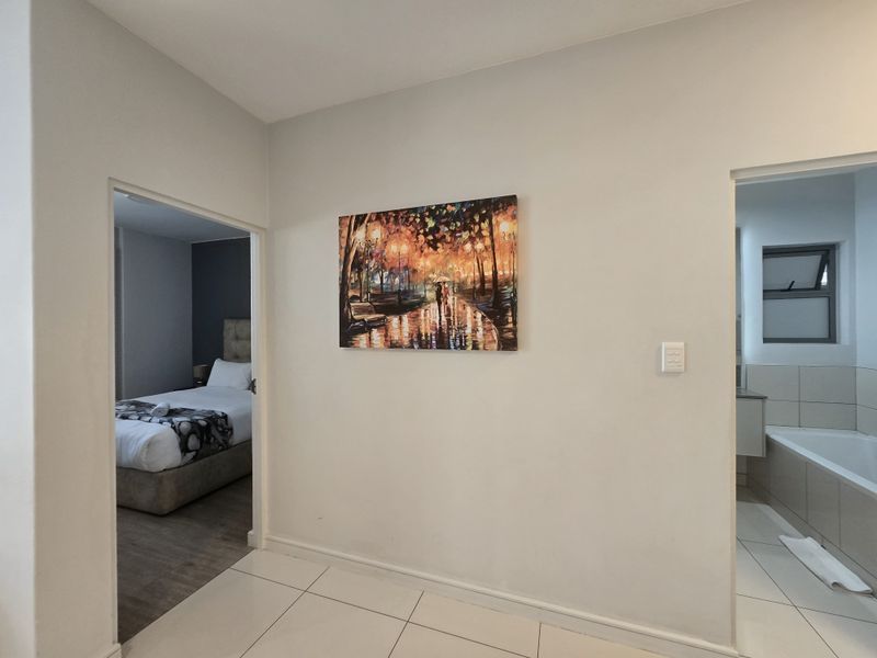 A clean, neutral hallway featuring tiled flooring, providing access to an adjacent bedroom and bathroom.