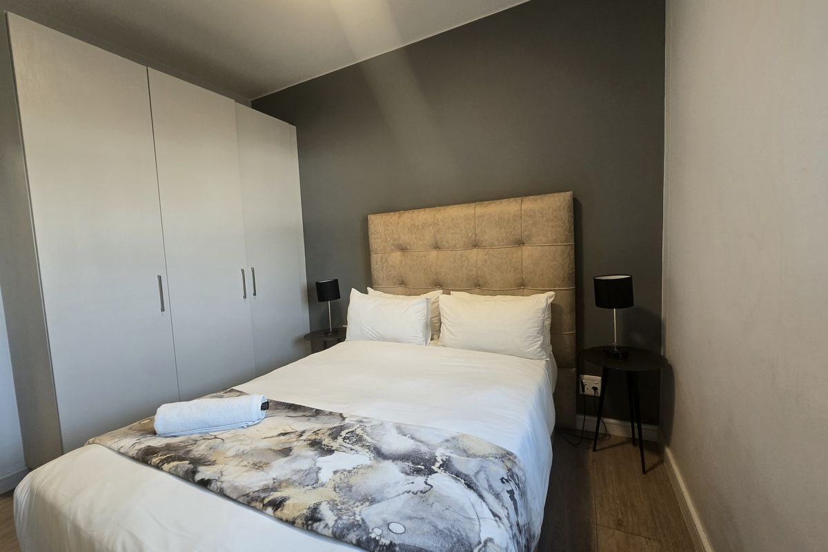 A well-maintained bedroom featuring laminate flooring, a dark grey accent wall, and a large built-in wardrobe for ample storage.