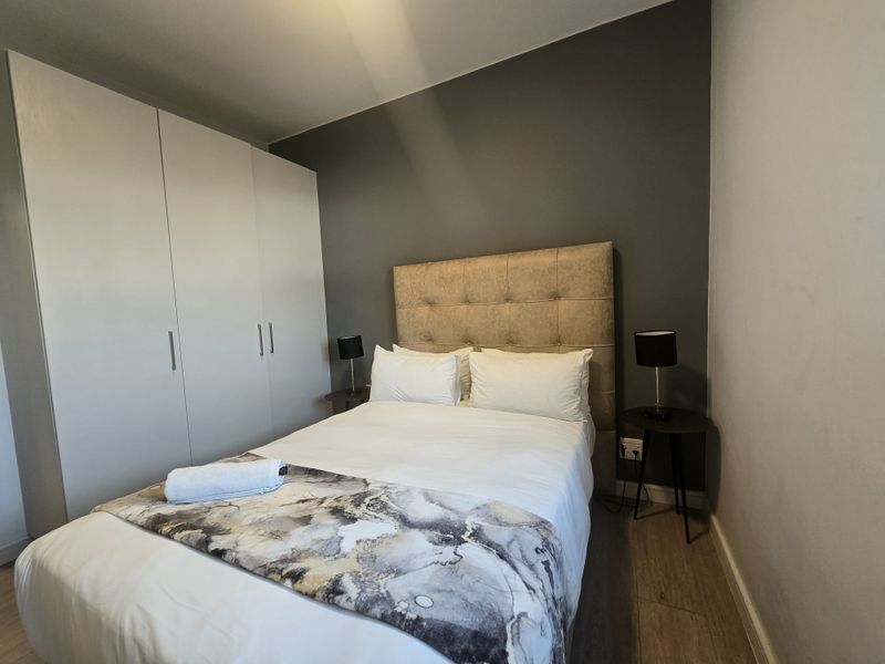 A well-maintained bedroom featuring laminate flooring, a dark grey accent wall, and a large built-in wardrobe for ample storage.