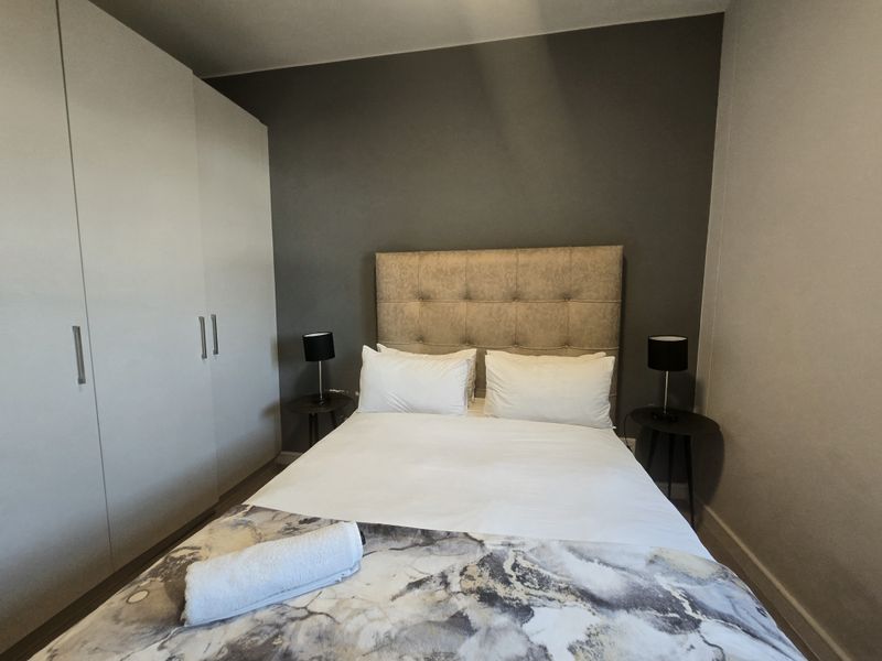 A well-maintained bedroom featuring a neutral color palette, a dark accent wall, and a large built-in wardrobe for ample storage.