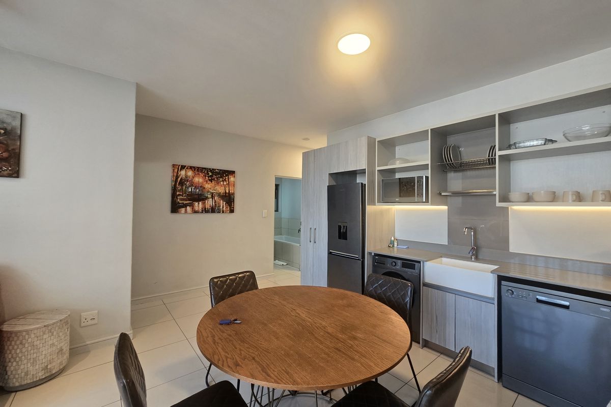 Modern open-plan kitchen featuring sleek cabinetry, a farmhouse sink, integrated appliances, and tiled flooring, seamlessly flowing into the dining area.