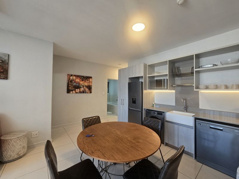 Modern open-plan kitchen featuring sleek cabinetry, a farmhouse sink, integrated appliances, and tiled flooring, seamlessly flowing into the dining area.