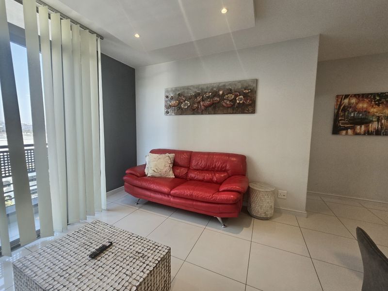 A bright living room featuring tiled flooring, recessed ceiling lights, and a large sliding glass door with vertical blinds leading to an outdoor area.