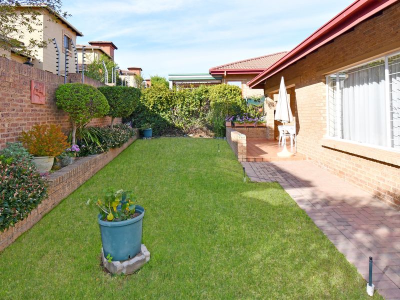 A well-maintained rear garden featuring a paved patio area, manicured lawn, raised brick planter beds, and secure perimeter walling with electric fencing.