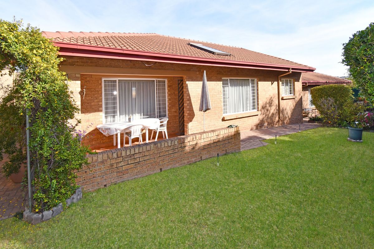 Rear view of a brick house featuring a covered patio, paved walkway, and a well-maintained lawn with a solar water heater on the roof.