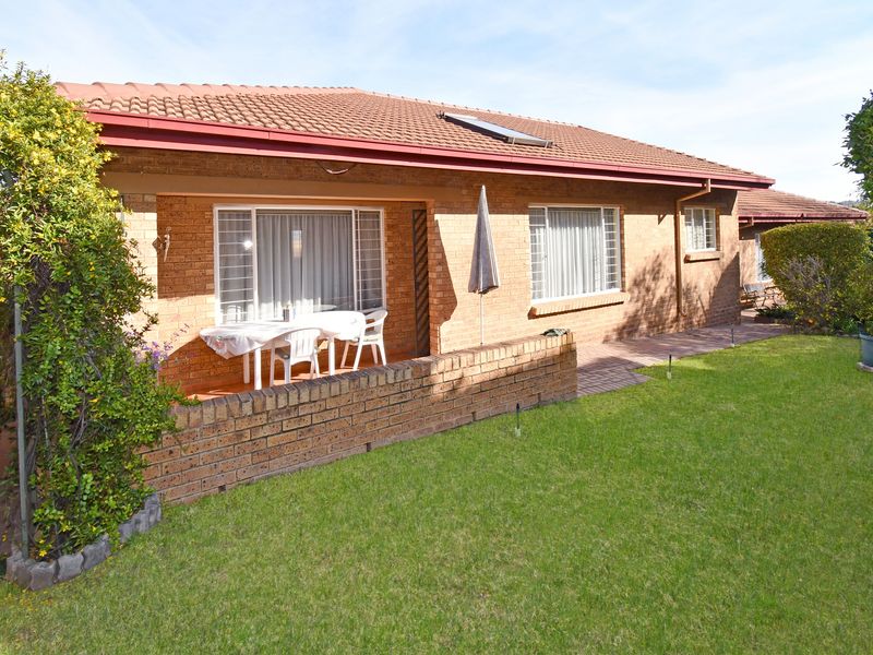 Rear view of a brick house featuring a covered patio, paved walkway, and a well-maintained lawn with a solar water heater on the roof.