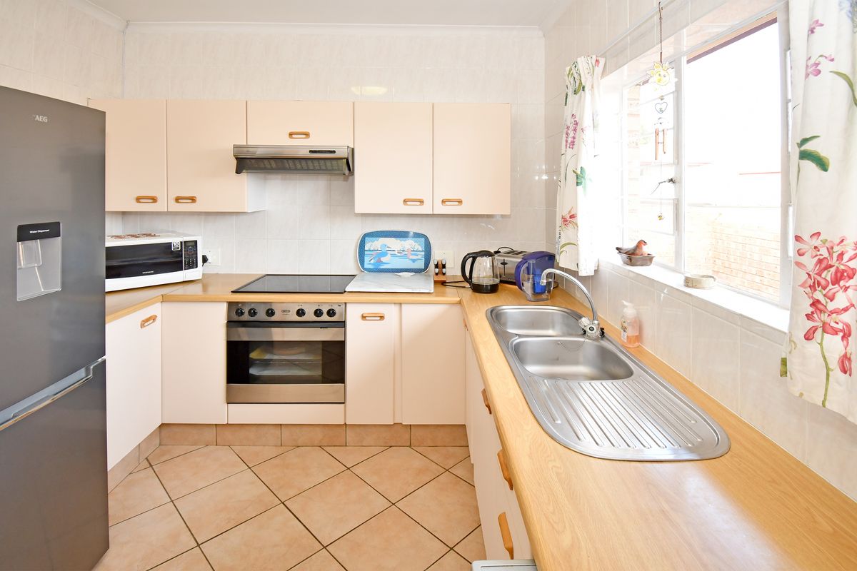 A functional kitchen featuring light-toned cabinetry, laminate countertops, a stainless steel double sink, and built-in cooking appliances with tiled flooring and splashbacks.