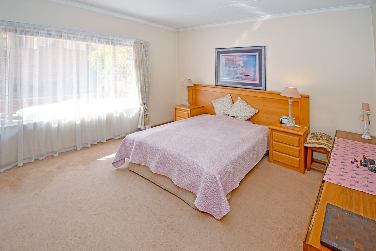 A spacious bedroom featuring neutral wall tones, carpeted flooring, and a large window allowing for ample natural light.