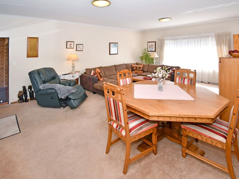Spacious open-plan living and dining area featuring neutral wall finishes, carpeted flooring, and large windows with curtain tracks.