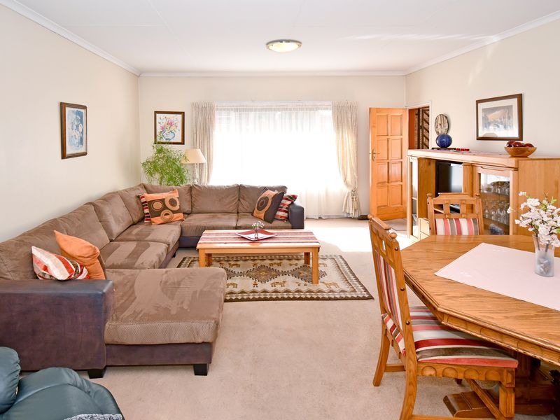 Spacious open-plan living and dining area featuring neutral wall finishes, carpeted flooring, and natural light through large window treatments.