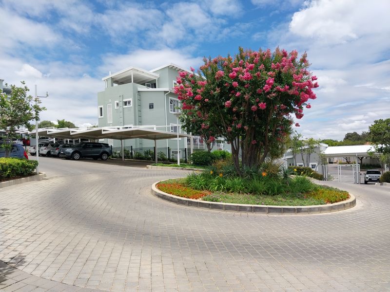 Exterior view of an apartment complex featuring a paved driveway, covered parking carports, and a well-maintained landscaped garden area.