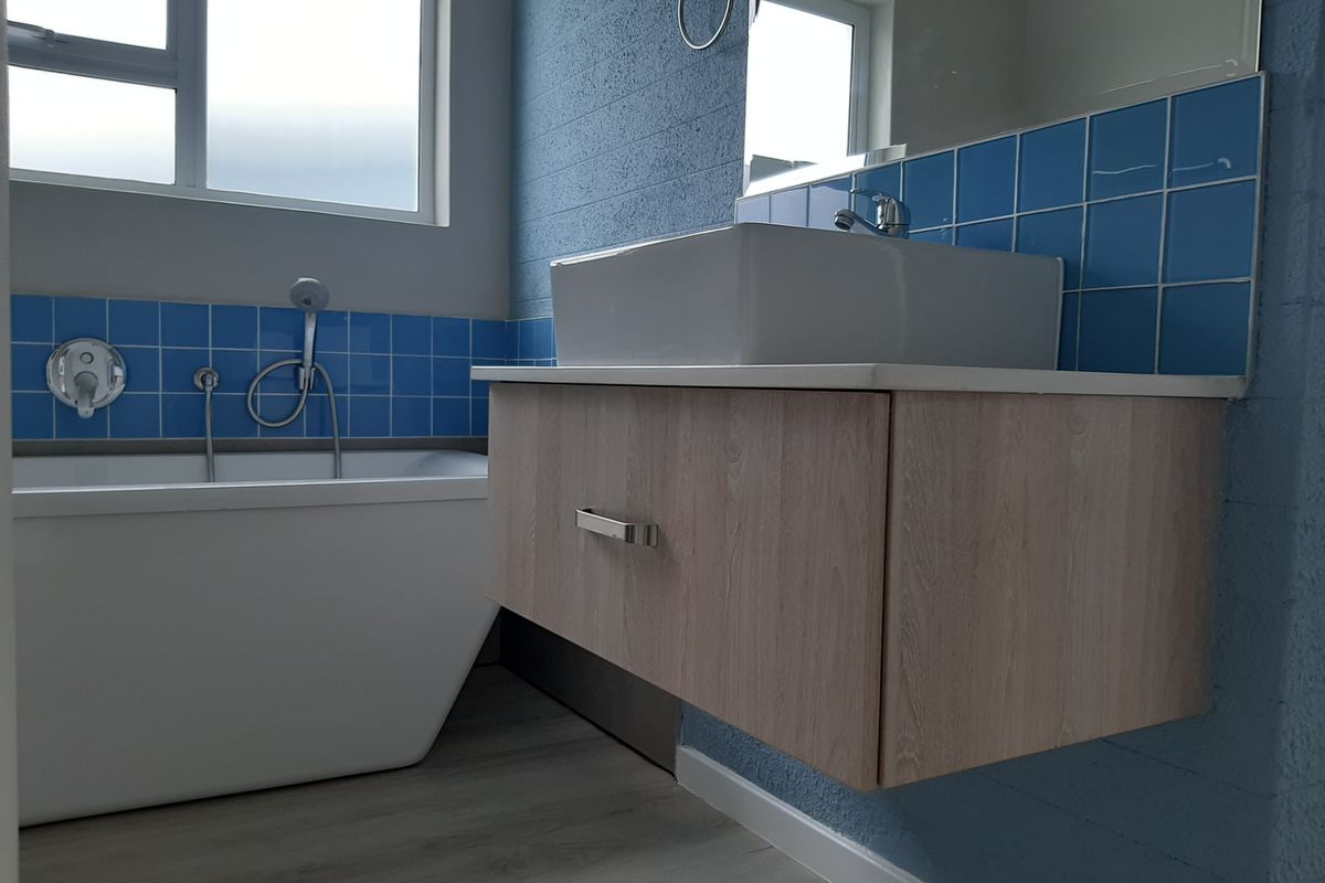 Modern bathroom featuring a floating vanity with a vessel sink, a sleek freestanding bathtub, and blue tiled splashbacks.