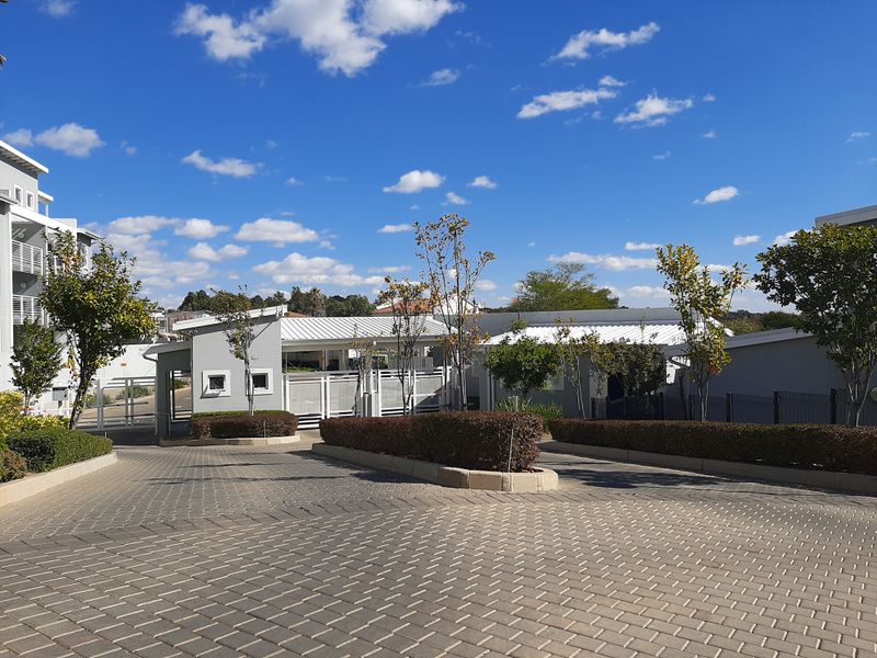 View of the apartment complex entrance featuring a paved driveway, security gate, and well-maintained guard house with landscaped hedging.