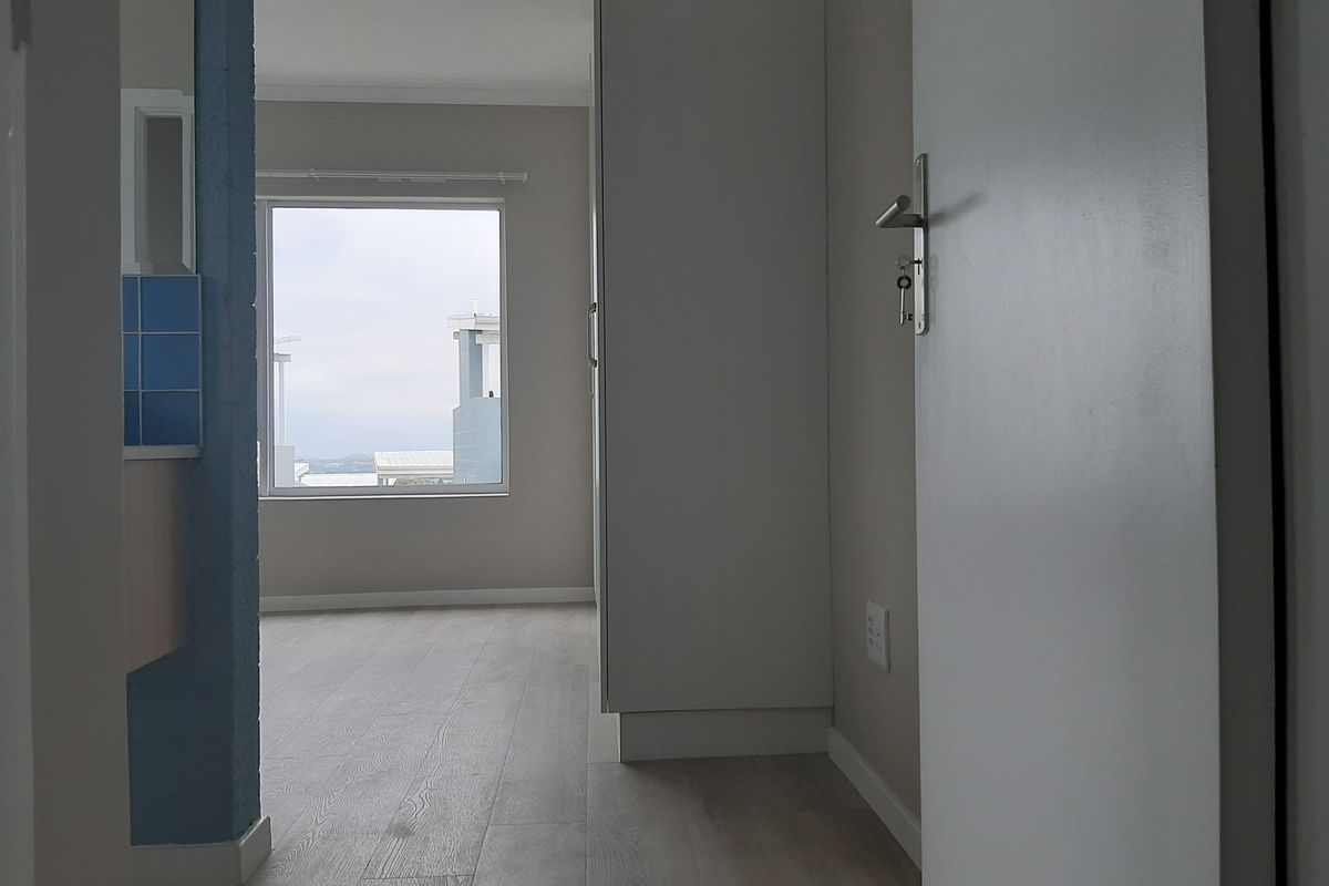 A bright, empty bedroom featuring light-toned laminate flooring, built-in cupboards, and a window with an exterior view.
