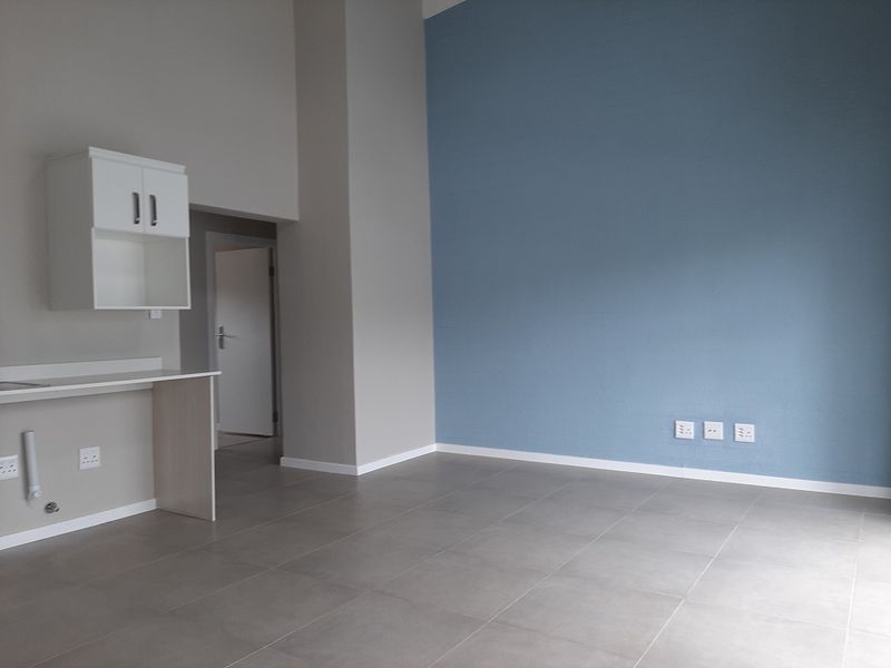 An empty open-plan living area featuring neutral tiled flooring, a blue accent wall, and a built-in kitchenette or utility counter.