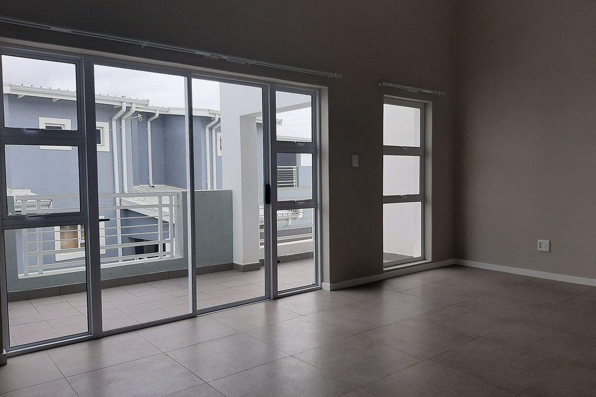 Spacious, empty living area featuring neutral tiled flooring and large aluminium sliding doors providing direct access to a private balcony.