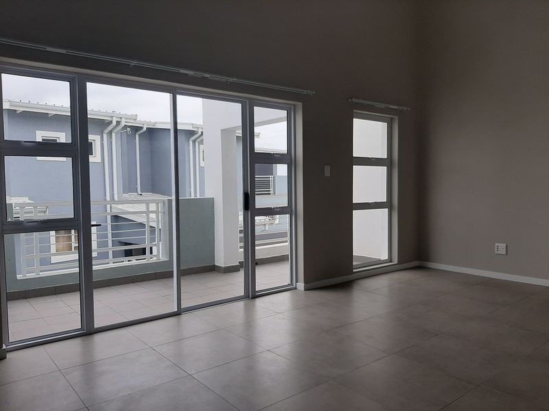 Spacious, empty living area featuring neutral tiled flooring and large aluminium sliding doors providing direct access to a private balcony.
