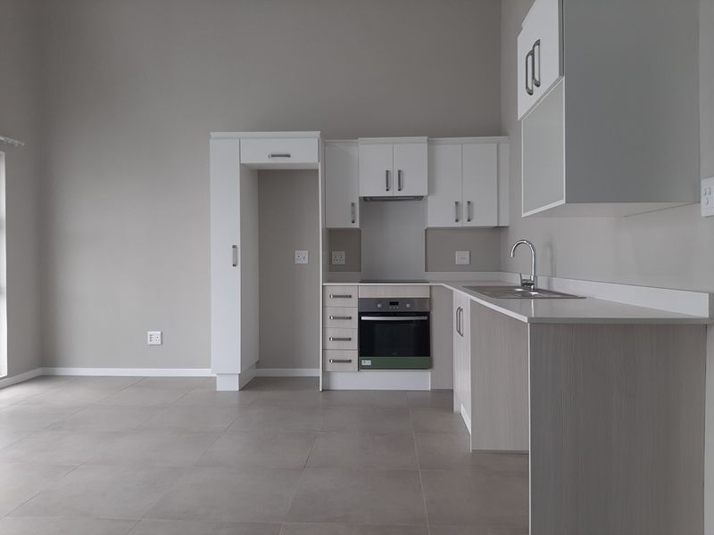 Modern, clean-lined kitchen featuring white cabinetry, integrated oven and hob, stainless steel sink, and neutral tiled flooring in an open-plan layout.