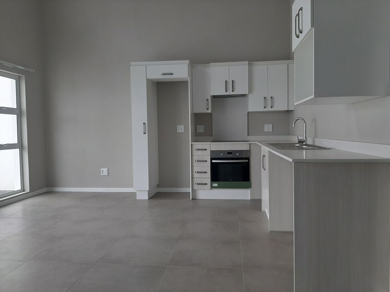 Modern open-plan kitchen featuring white cabinetry, built-in oven and hob, stainless steel sink, and neutral tiled flooring in a bright, spacious living area.