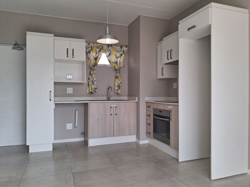 A clean, modern kitchen featuring built-in cabinetry, a stainless steel sink, integrated oven, and neutral tiled flooring in an open-plan layout.