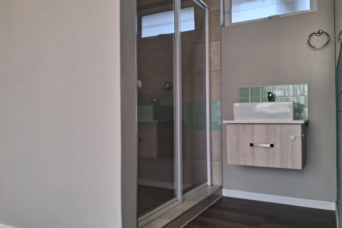 A modern bathroom featuring a glass shower enclosure, a wall-mounted vanity with a vessel sink, and neutral wall finishes with tiled accents.