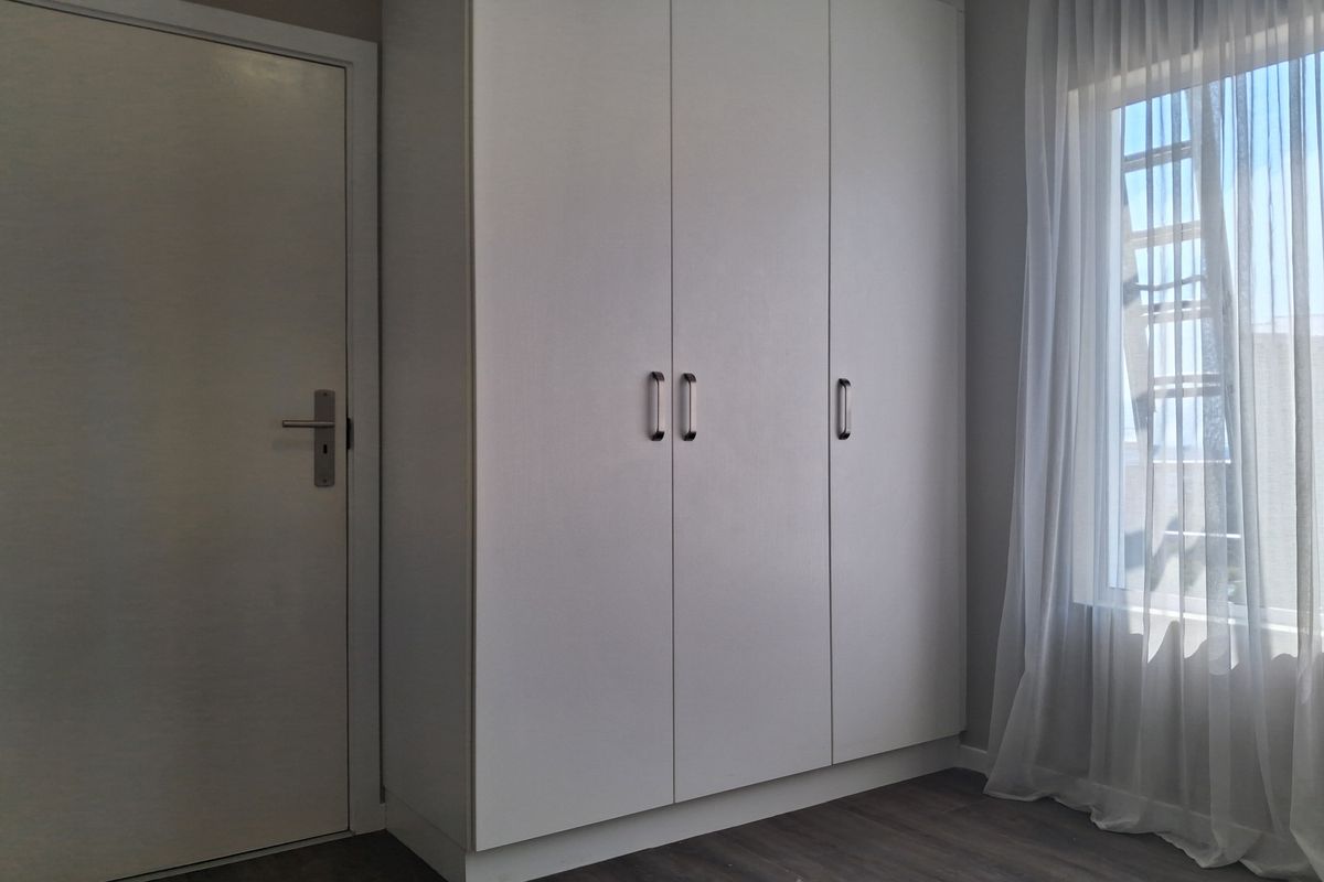 A clean, modern bedroom featuring neutral tones, built-in wardrobe storage, and durable laminate flooring with natural light.