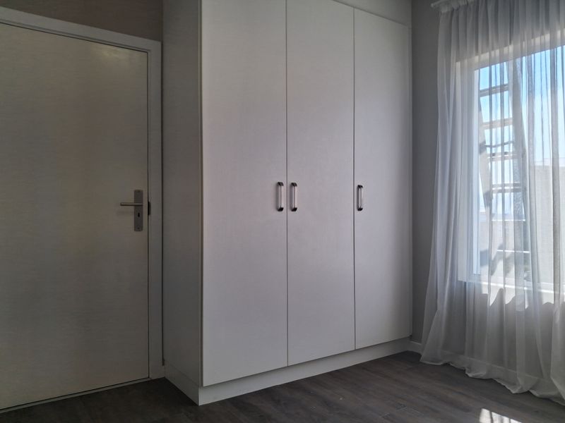 A clean, modern bedroom featuring neutral tones, built-in wardrobe storage, and durable laminate flooring with natural light.