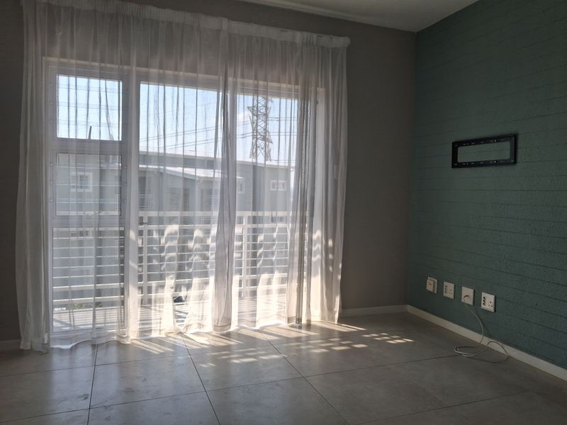 A bright, empty living room featuring large sliding glass doors, tiled flooring, and a teal accent wall with integrated electrical points and TV mounting bracket.