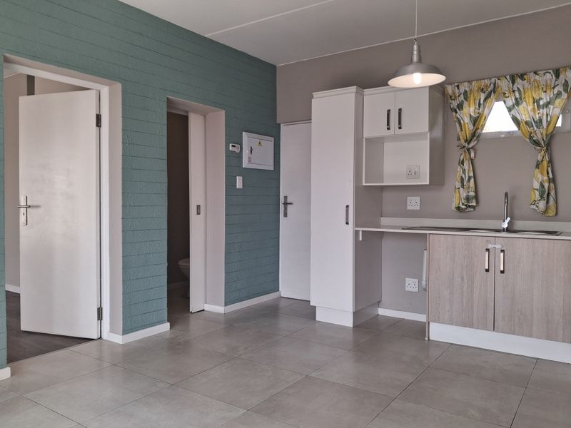A clean, functional kitchen area featuring neutral cabinetry, tiled flooring, and a stainless steel sink, with direct access to adjacent rooms.
