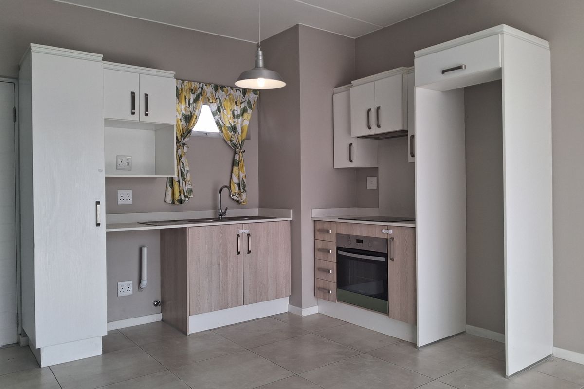 A clean, modern kitchen featuring light wood-tone cabinetry, white overhead cupboards, built-in oven and hob, and neutral tiled flooring.