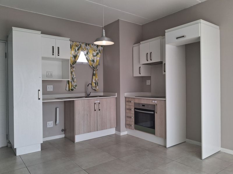 A clean, modern kitchen featuring light wood-tone cabinetry, white overhead cupboards, built-in oven and hob, and neutral tiled flooring.
