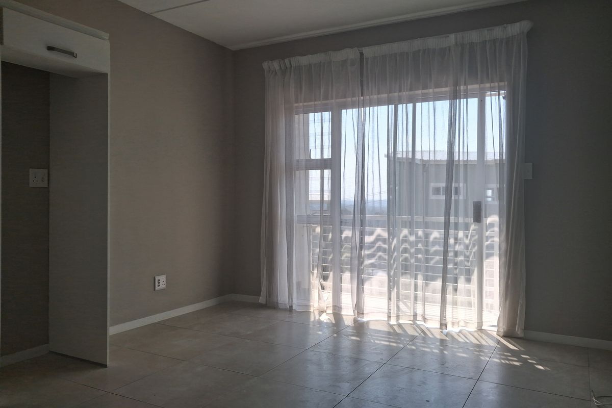 A bright, empty living area featuring neutral tiled flooring and a large sliding glass door that provides access to an outdoor balcony.