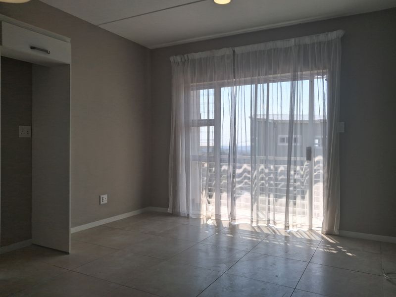 A bright, empty living area featuring neutral tiled flooring and a large sliding glass door that provides access to an outdoor balcony.