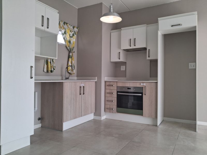 A clean, modern kitchen featuring light wood-tone cabinetry, built-in oven, extractor fan, stainless steel sink, and neutral tiled flooring.
