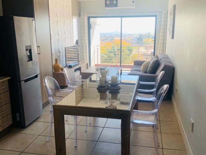 Open-plan living and dining area featuring tiled floors, a textured feature wall, and a sliding door leading to a balcony with scenic views.