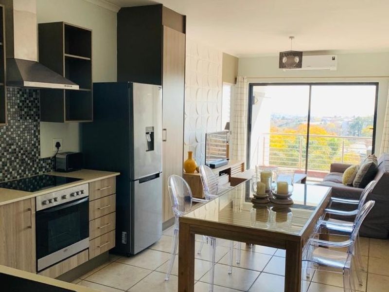 Modern open-plan kitchen and dining area featuring tiled floors, built-in cabinetry, integrated appliances, and direct access to a balcony with scenic views.